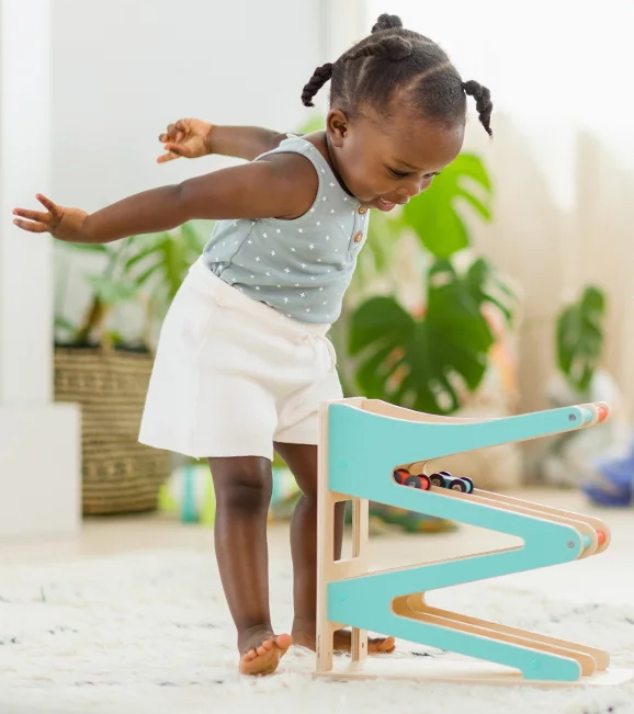 "Toddler girl playing with wooden race car track"