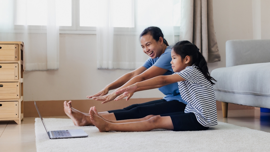 "mom and daughter sitting on the floor stretching and doing an online exercise class"