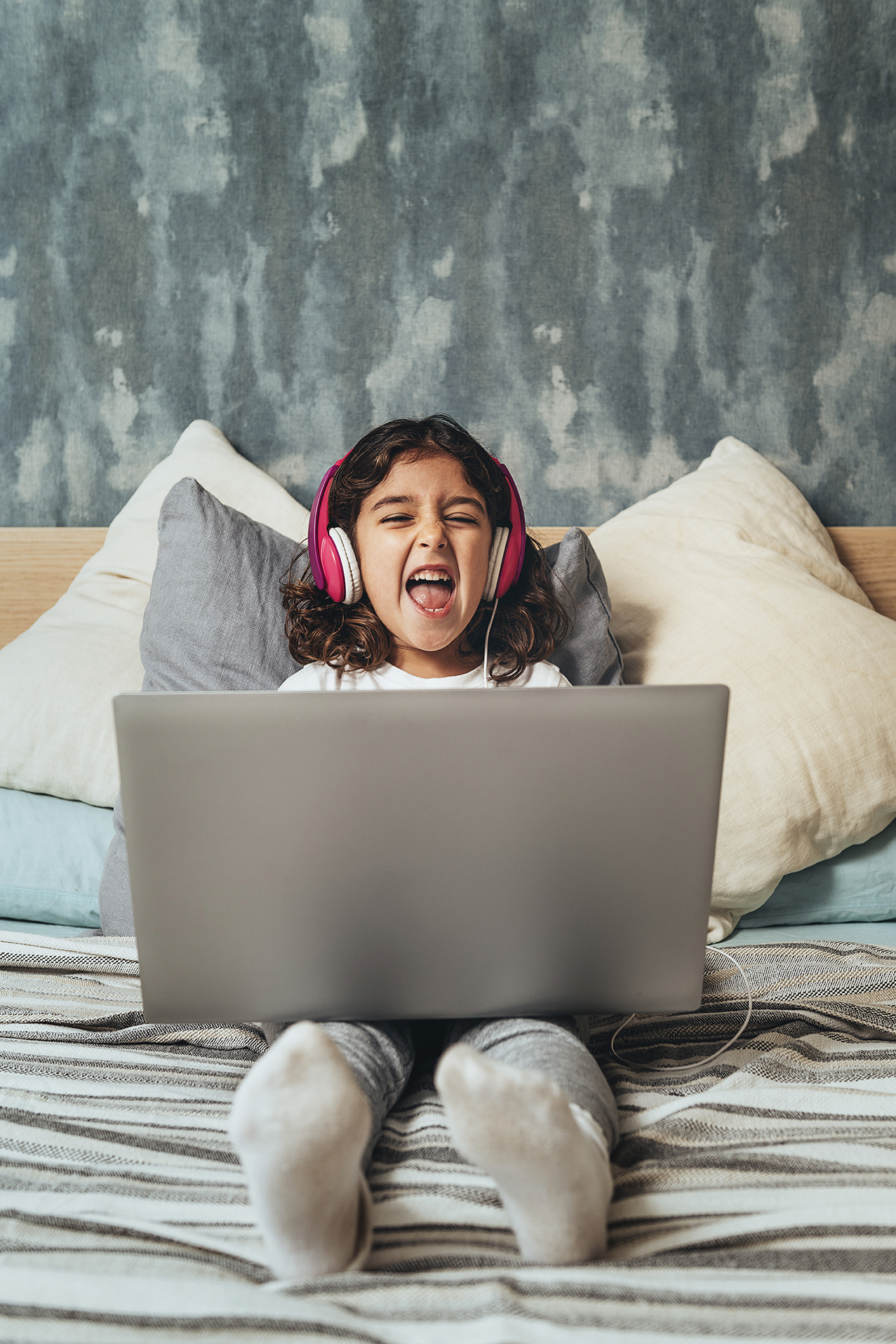 "Little girl watching tv on a laptop, laughing and wearing pink headphones"