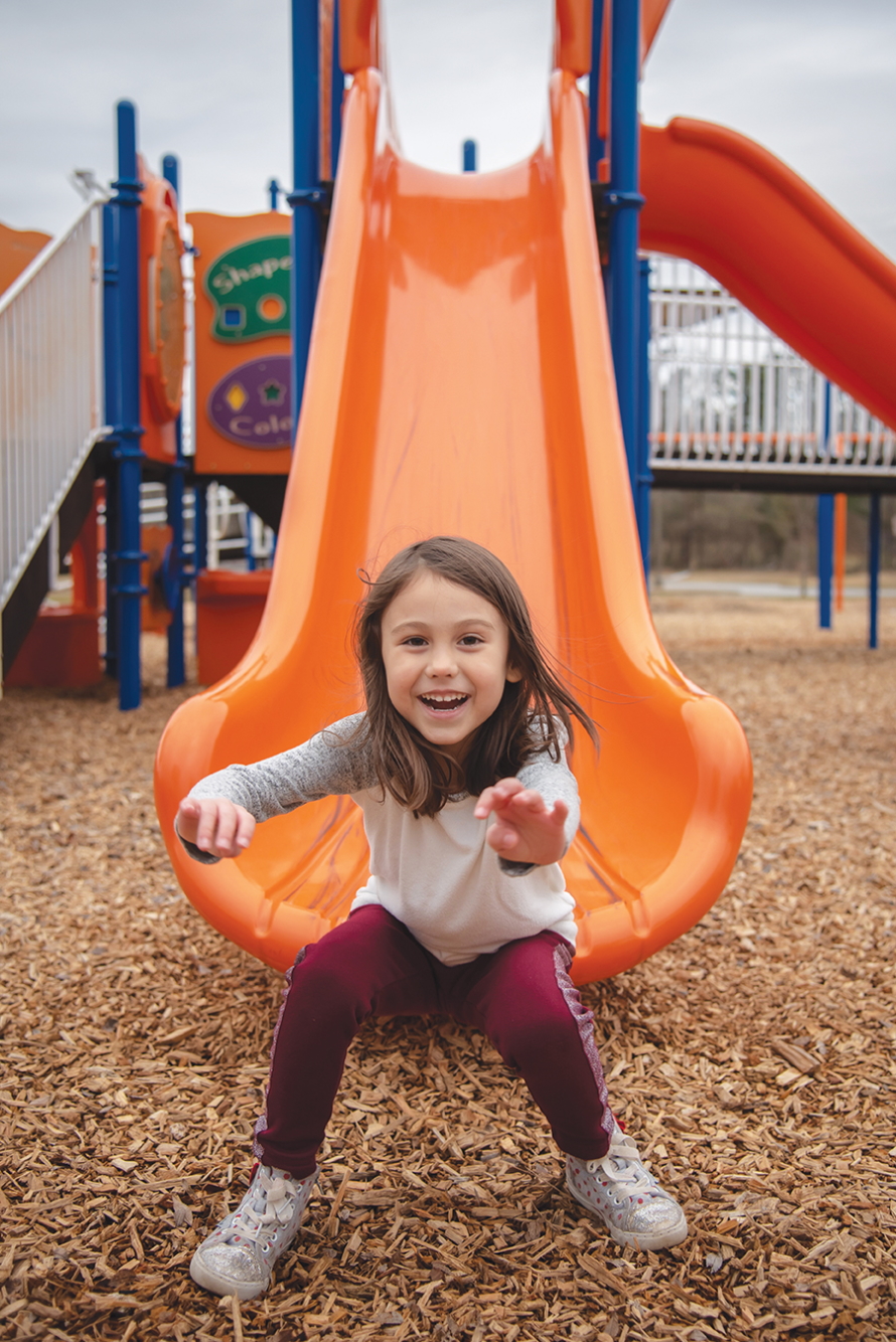 "Smiling little girl at the bottom of a slide"