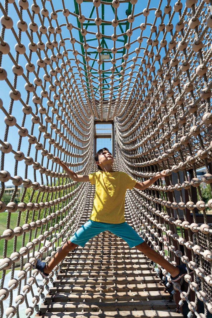 "Young boy crossing a rope bridge holding onto the sides"