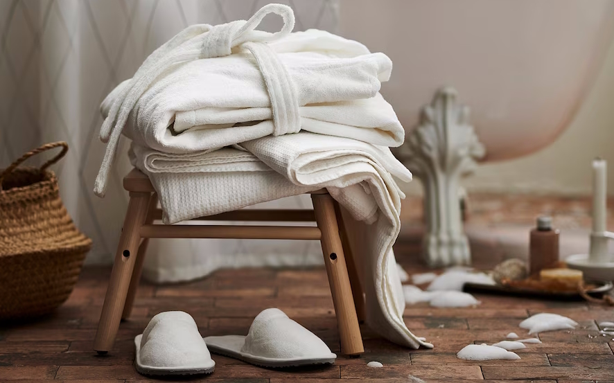 white bathrobe and slippers sitting on a wooden bench are hosting essentials from ikea