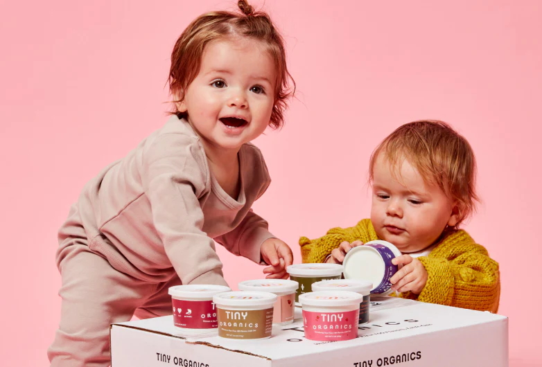"Two babies holding containers of Tint Organics baby food"