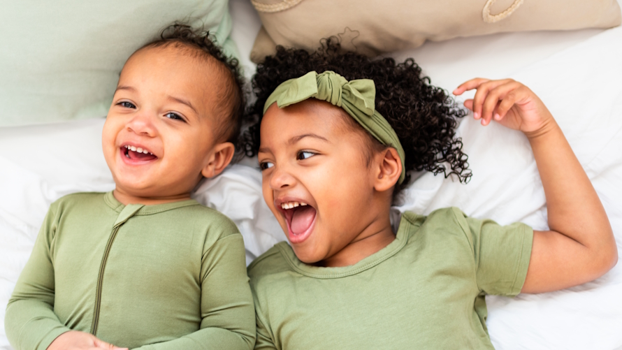 "Two young children lying on a bed in green pajamas laughing"