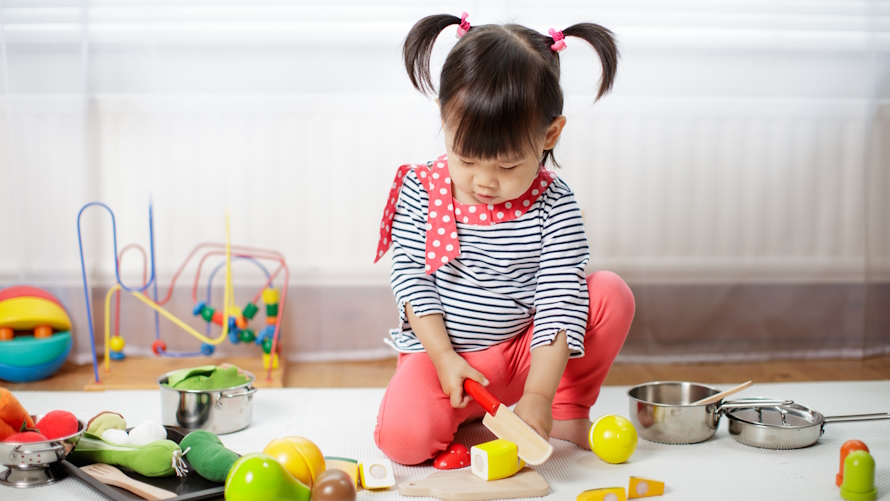 "Young girl sitting on the floor pretending to make food"