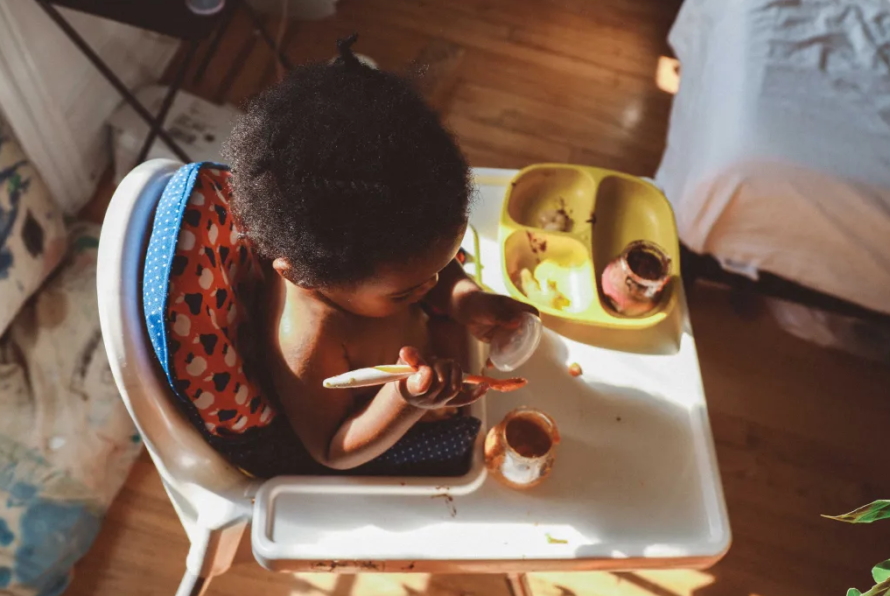 "Baby eating baby food out of a jar in a highchair"
