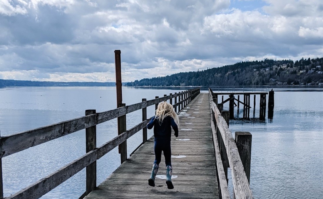 Girl jumping on Point White Pier on Bainbridge Island, Washington, near Seattle exploring with activity kit from KiDiMu