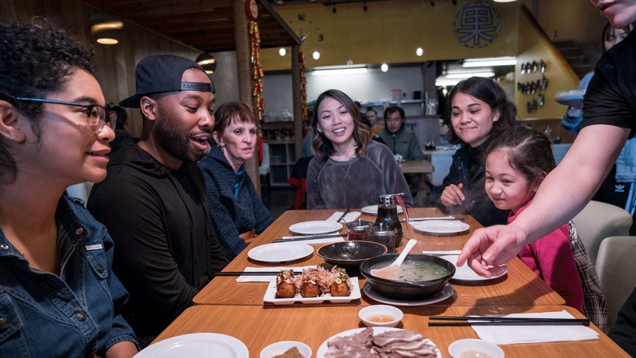 people on a food tour in seattle sitting around a table with soup and Asian food