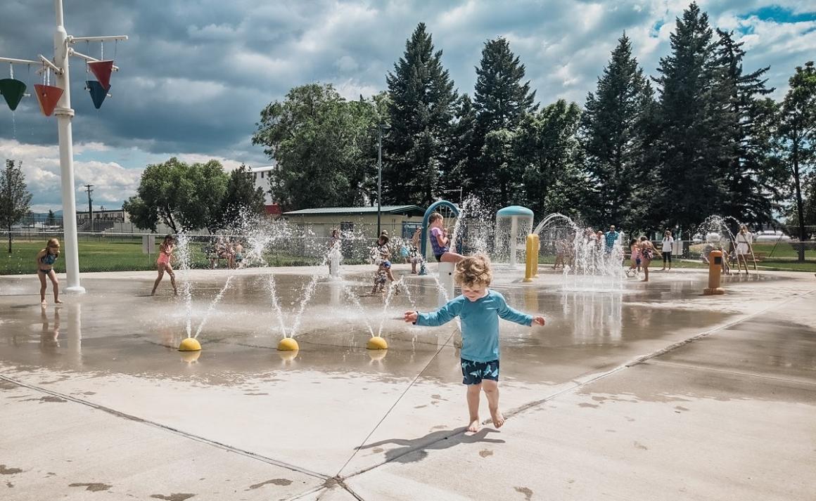 Child playing at a spray park on a summer day on a kid-friendly play stop of a family camper van life road trip