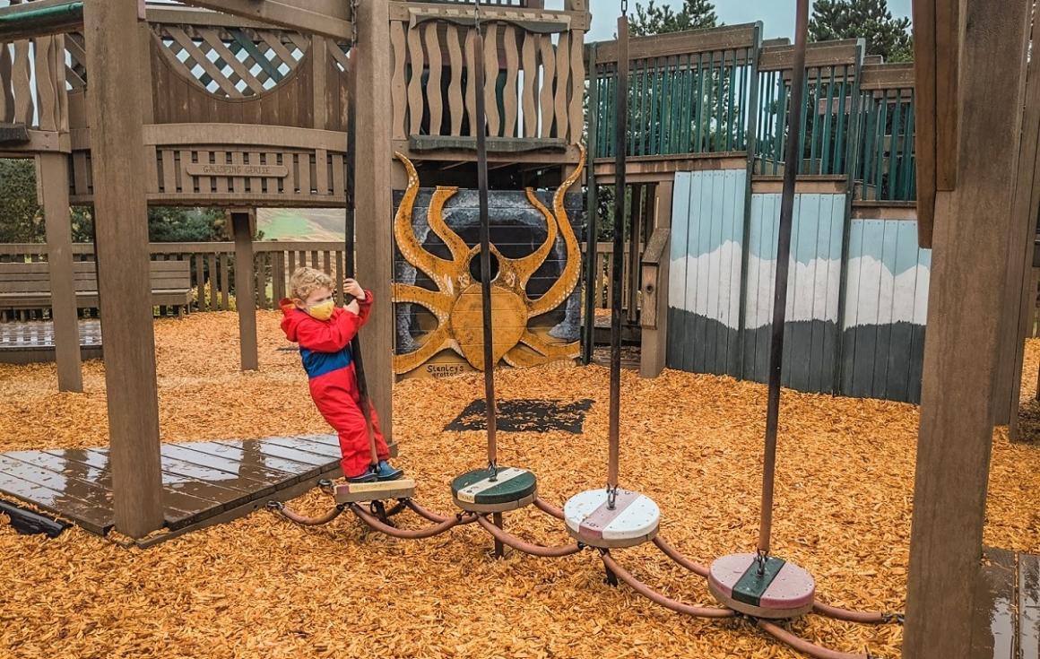 Young boy in red rain suit playing at  Chambers Bay Regional Park's Playground by the Sound he is balancing on a play element