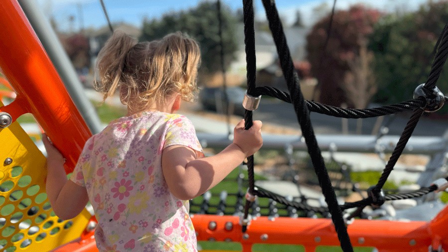 young girl at the top of a playground structure looking down at the park in Seattle
