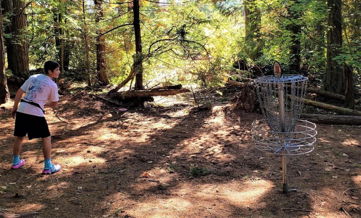 A boy about age 13 throws a disc toward a disc golf hole at Gaffney's Grove a disc golf course near Seattle in one family's first time trying this fun and free family sport