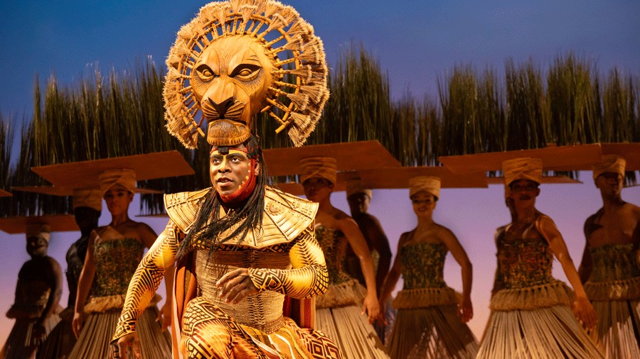 Mufasa dances onstage in front of grass during a stunning Lion King musical performance