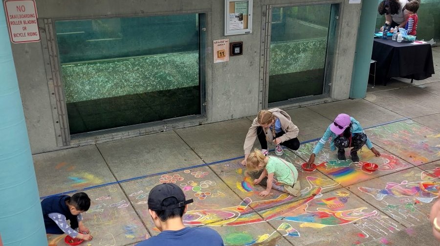 Kids draw colorful salmon chalk art in front of salmon fry tanks at the Issaquah Salmon Hatchery for Earth Day.