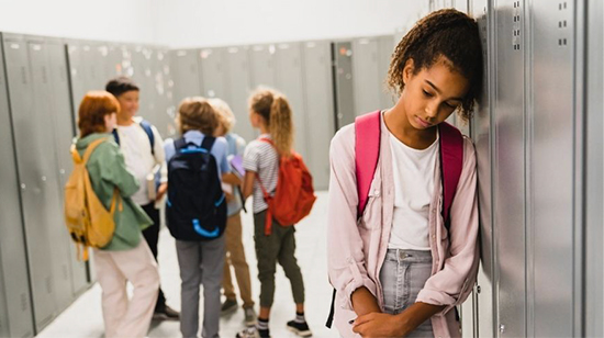 Middle school girl in hallway with sad expression putting her head against a locker