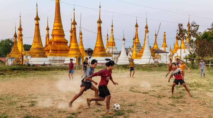 Asian boys play soccer with golden temples in the background.