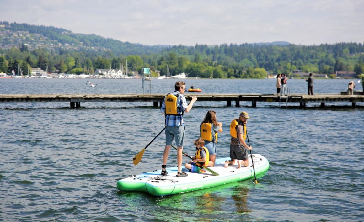 Family enjoying a paddle on a six-person stand-up paddleboard from the REI boathouse at Enatai Beach near Seattle best family activities for summer tourists