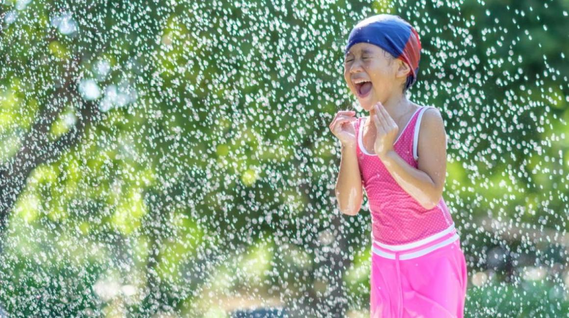 Girl playing in the backyard in the sprinkler to keep cool during a Seattle heat wave