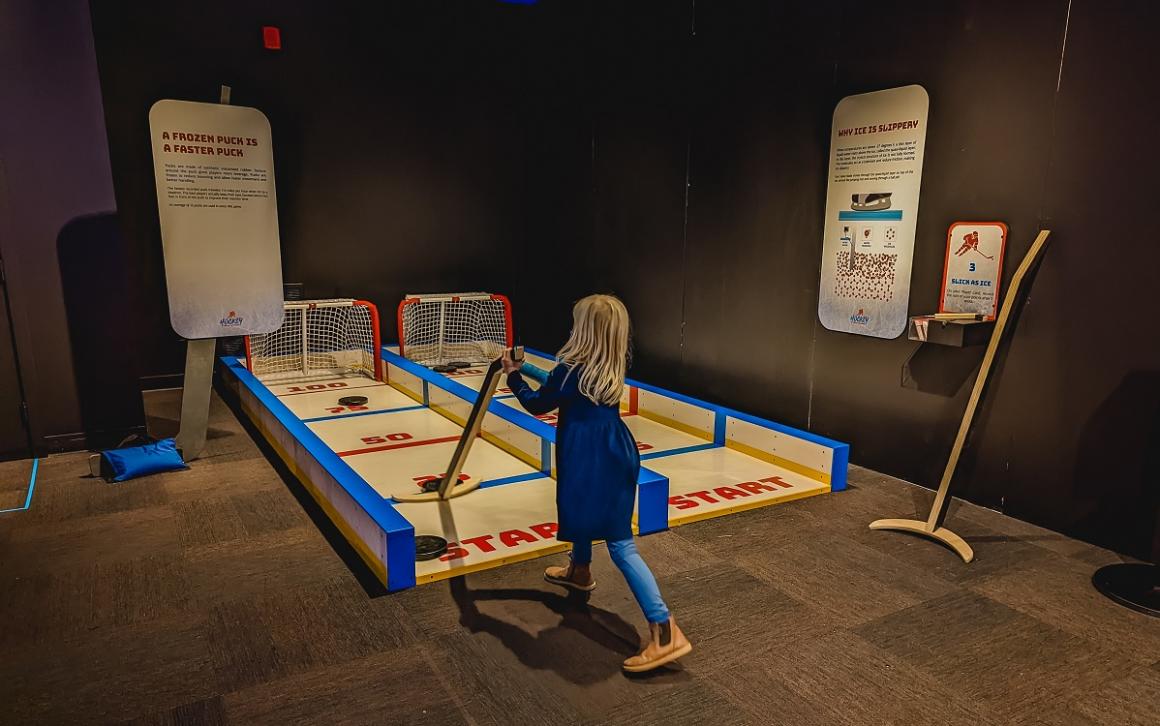 A young girl plays with a shuffleboard-style hockey game to test puck travel at Pacific Science Center's Hockey: Faster Than Ever interactive exhibit