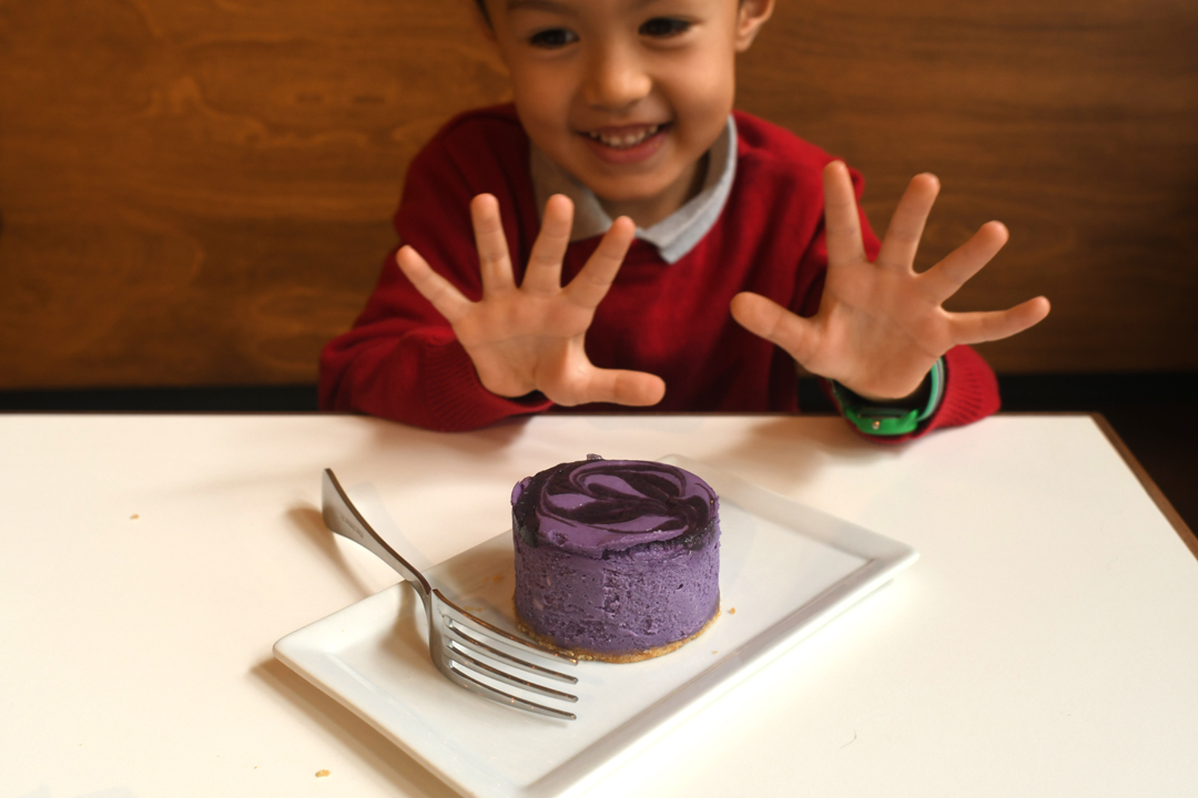 A happy kid abou to eat a mini purple cheesecake made of ube from Hood Famous Cafe in Seattle