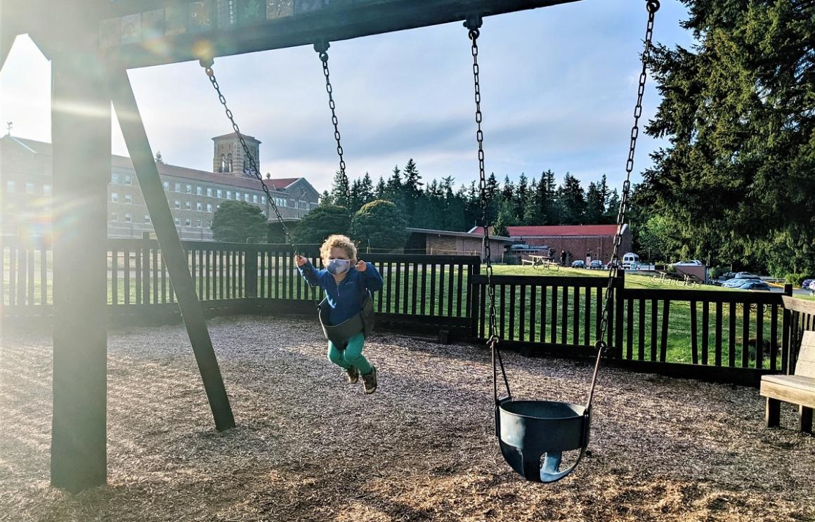 Playground swings with boy swinging in the foreground, lodge at St. Edward State Park behind new Seattle upscale lodge former seminary