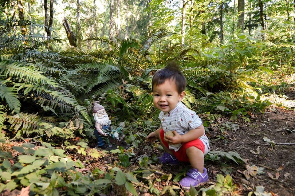 Very small and cute boy crouching next to gnome along the Maple Valley gnome trail