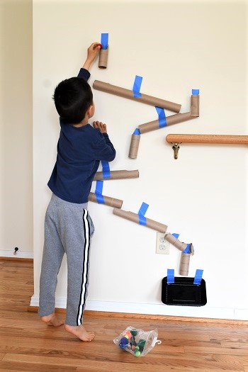 boy playing with toilet paper tube marble run taped to wall during short at home recess break remote learning
