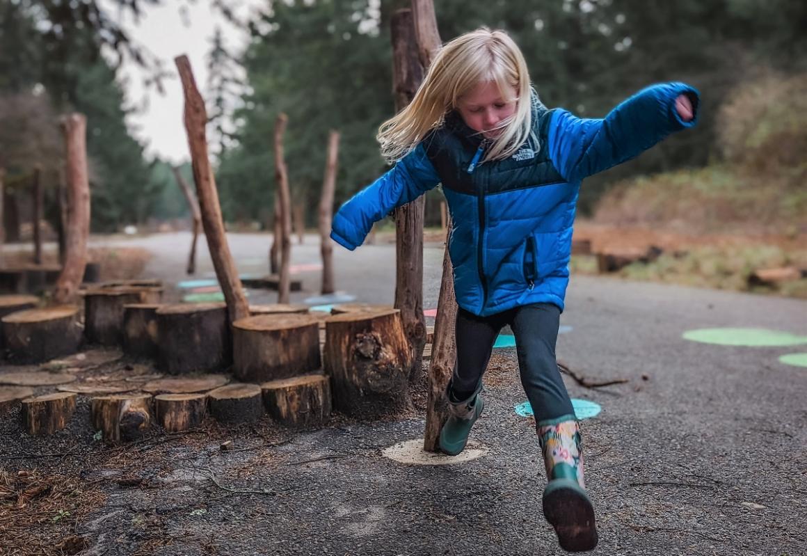 Girl jumping from stump to circle at Pause and Play play area updated Swan Creek Park Tacoma's Eastside