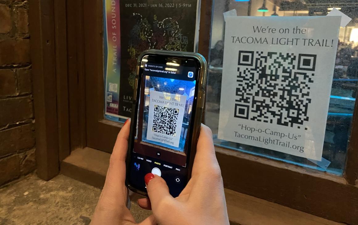 View of hands holding a phone and reading a QR code along the Tacoma Light Trail. QR codes access sound and additional information about each art piece.
