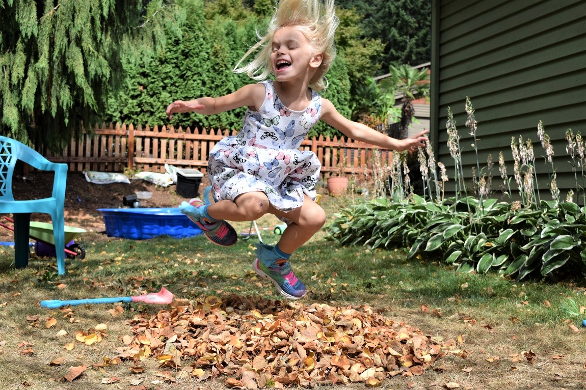 Girl jumping happily in a pile of leaves in her yard can outdoor time raise your happiness ranking