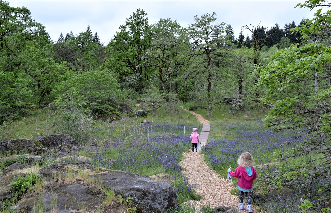 Two young girls in jackets walking a path through a beautiful green nature area creating a soundmap virtual travel activities