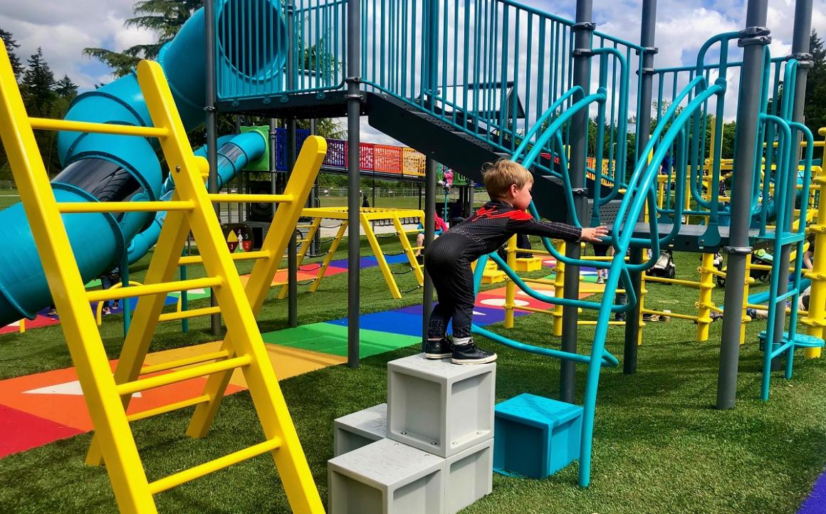 Small boy in spiderman shirt climbing on play features at the colorful new playground at West Fenwick Park in Kent near Seattle