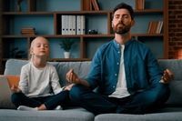 Dad and young daughter meditating on couch at home