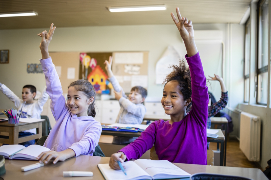 two girls in a classroom raising their hands