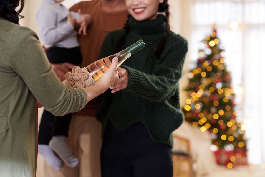woman handing another woman a bottle of wine as a holiday gift 