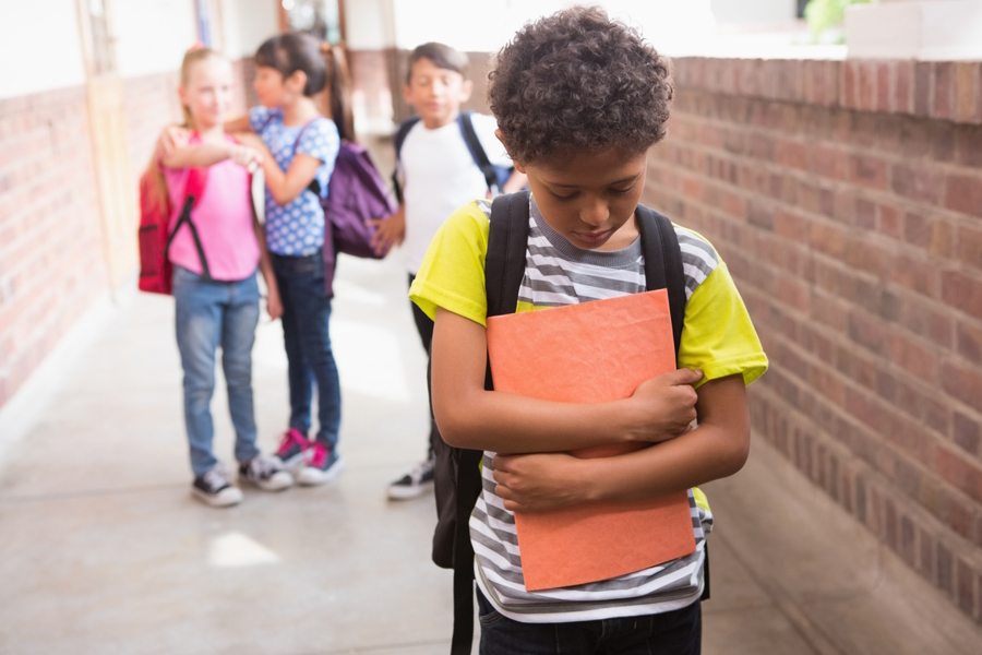 boy holding school folder and looking down while other kids point and laugh at him