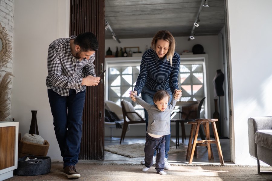 Little boy walking while mom holds his hands and dad films with his cell phone