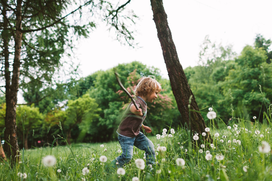 young boy walking through a field with a stick