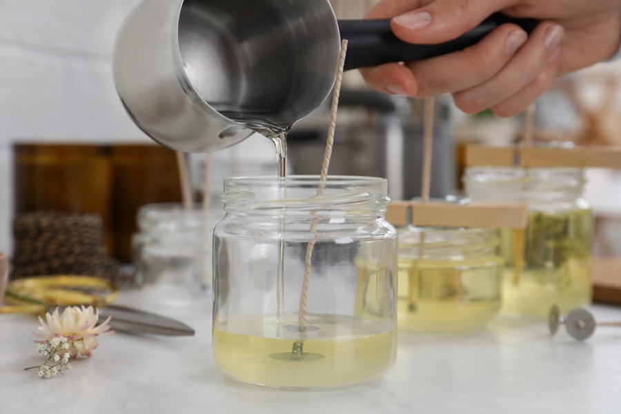 pouring wax from a pot into a glass jar for a candle 