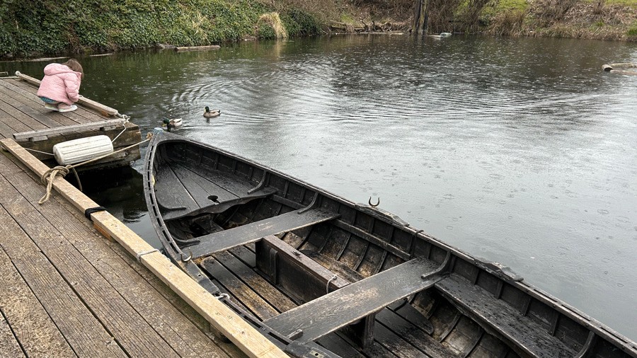 free peapod rowboat by the dock with ducks swimming by and a young girl watching