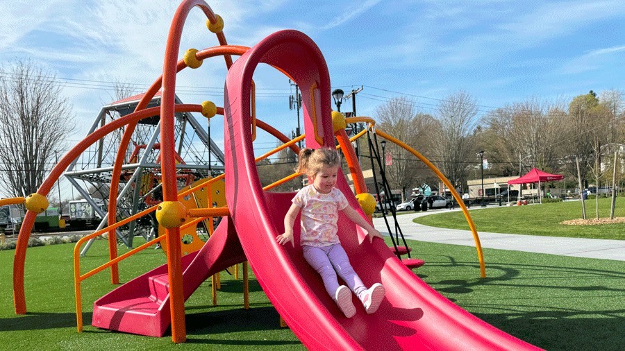 young girl sliding down a red slide on the playground at Cheryl Chow Park
