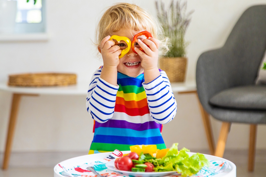 Child holding up veggies by her eyes eating color healthy foods