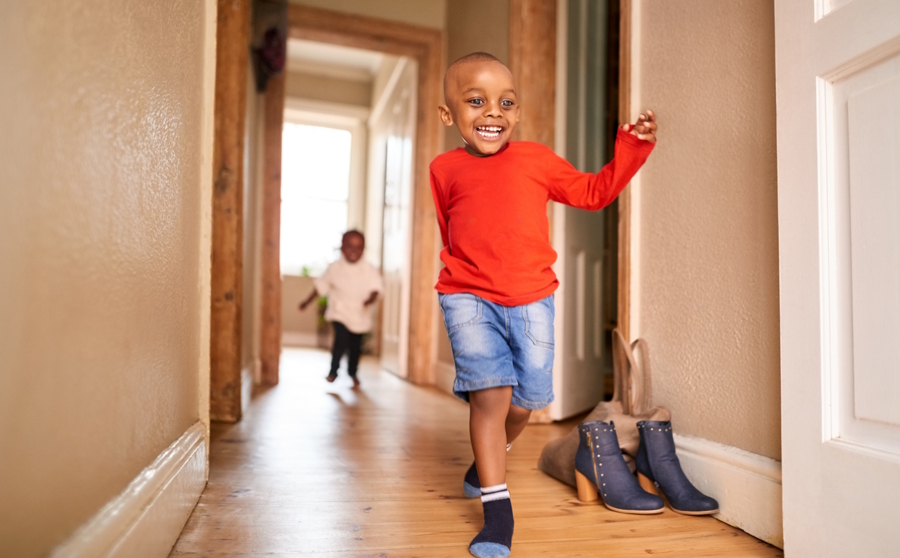 Boy running down a hallway in socks, pretending to ice skate at home