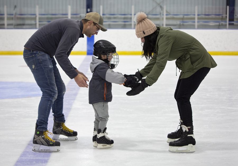 child on an ice rink with parents helping him stand