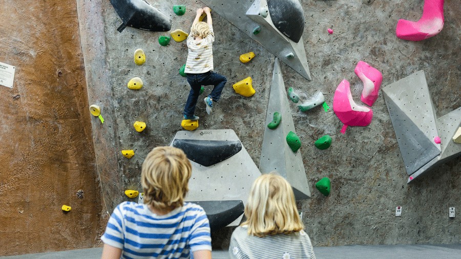 kids watching a boy climb on an indoor rock climbing gym wall in Seattle