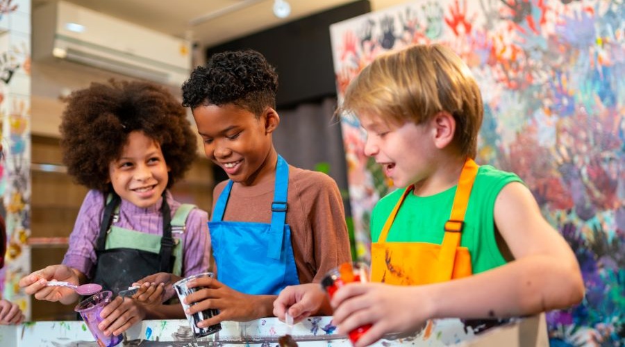 Two boys and a girl hold cups of paint as they create art.