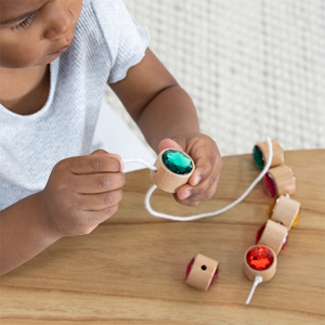 a child lacing blue and red gemstone beads on string christmas gift idea