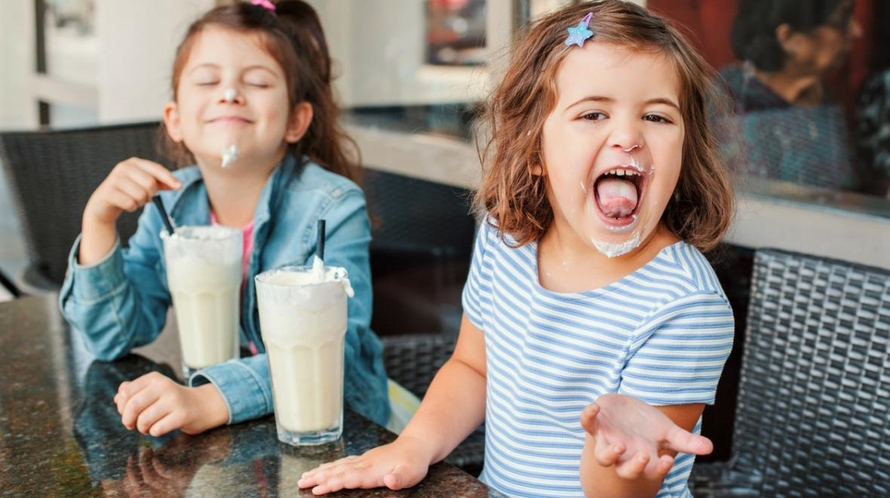 Two girls drinking a milkshake and smiling in a retro restaurant