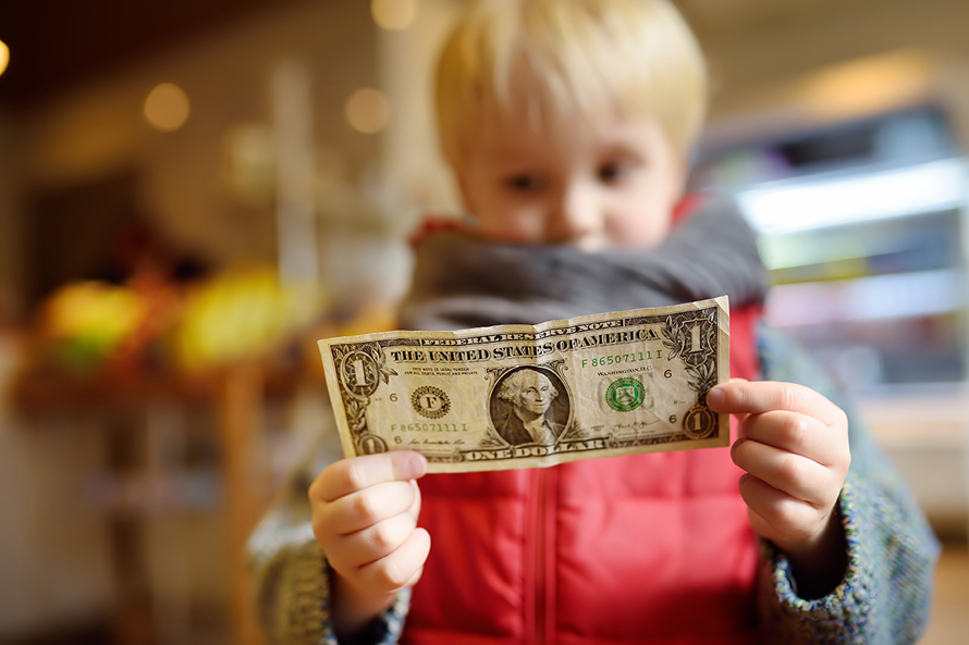little boy in a red jacket holding a dollar bill