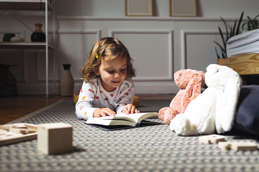 little girl reading on the floor in her bedroom with stuffed animals